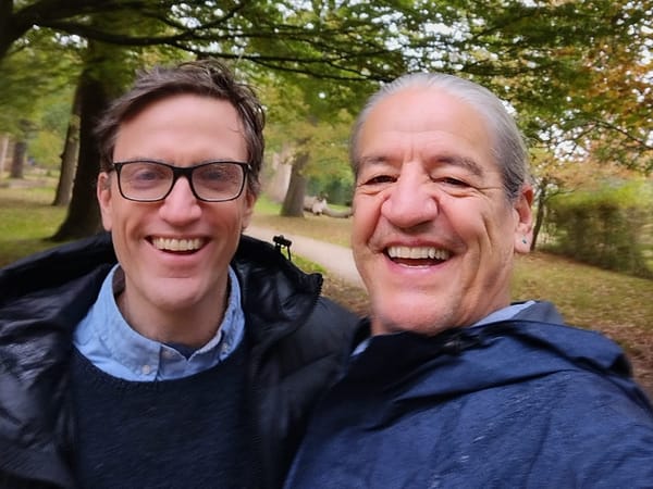 Two smiling men on wet day in a park.